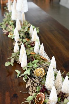 a long table is decorated with white cones and greenery, oranges and dried berries