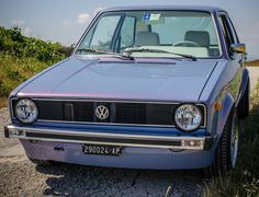 an old blue car parked on the side of a road next to grass and bushes