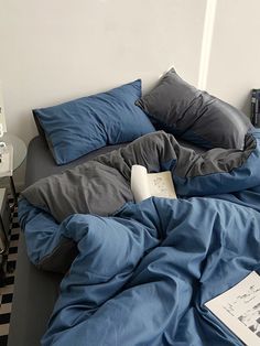 an unmade bed with blue sheets and pillows on it in a room that has black and white checkered flooring