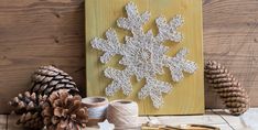 a snowflake made out of yarn sitting on top of a table next to some pine cones