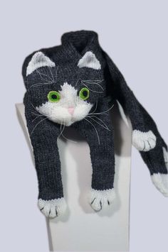 a knitted black and white cat hat on top of a stand with green eyes