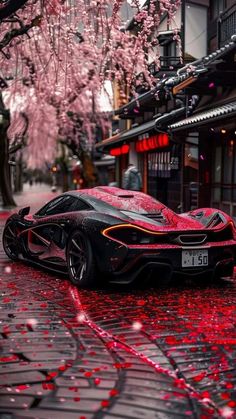 a red and black car parked on the side of a road next to cherry blossom trees