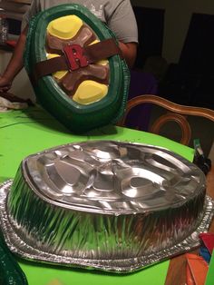 a man standing next to a cake pan on top of a green table covered in foil