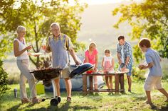 a group of people standing around a bbq grilling food on top of a grass covered field