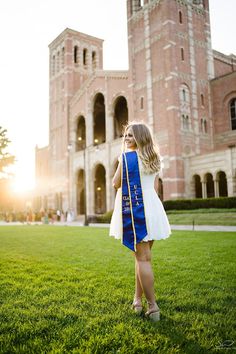 a woman in a blue and white graduation gown is standing on the grass near an old brick building