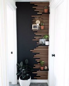 a black wall with wooden slats on it and some potted plants in the corner