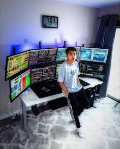 a young man sitting in front of multiple computer monitors on top of a white desk