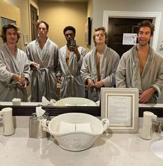 four men in robes standing in front of a bathroom mirror with a framed photograph on the counter