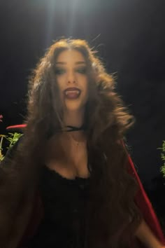 a woman with long hair wearing a red cape and posing for a photo in the dark