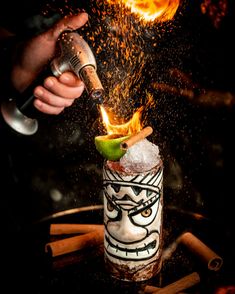 a person is pouring something into a glass with a lime on the side and fire coming out of it