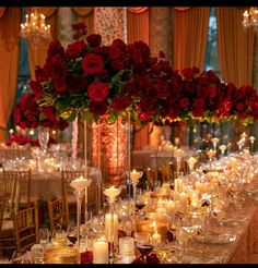 a long table is set with candles and roses in tall vases for centerpieces