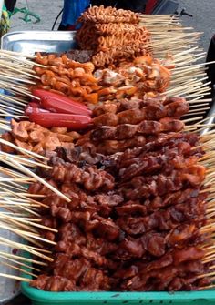 several skewered meats and vegetables on sticks in a green tray at an outdoor market