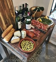 a wooden table topped with lots of different types of food and bottles of wine on top of it