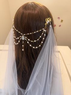 a bridal headpiece with pearls and beads on the side, sitting on top of a white veil