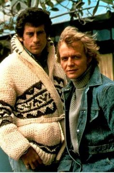 two men standing next to each other wearing sweaters