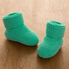 a pair of green knitted baby booties sitting on top of a wooden table