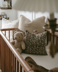 a teddy bear sitting on top of a crib next to pillows