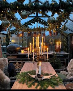 a dining room table with candles and christmas decorations on the top, surrounded by greenery