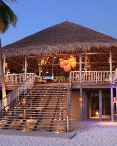 a beach side restaurant with stairs leading up to the roof and palm trees around it