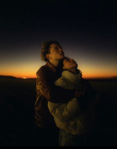 a man holding a woman in his arms as the sun sets behind him and she is looking up into the sky