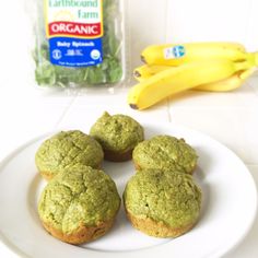 four green muffins on a white plate next to some bananas and a bag of organic