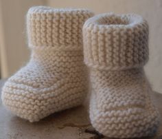 a pair of white knitted baby boots sitting on top of a wooden table next to a door