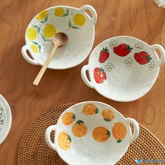 three bowls with fruit painted on them are sitting on a table next to a wooden spoon