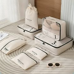 four pieces of white luggage sitting on top of a bed next to two pairs of sunglasses