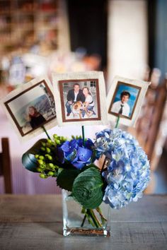 a vase filled with blue flowers sitting on top of a wooden table next to pictures