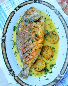 grilled fish with lemon sauce on a white and blue plate next to sliced tomatoes