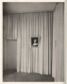 an old black and white photo of a woman looking out the window from behind curtains