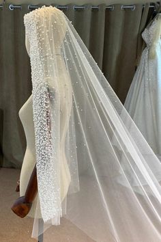 a wedding veil is hanging up on a mannequin in front of some dresses