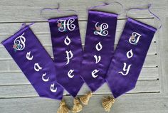 three purple banners with white letters and tassels hanging on a wooden wall next to two tassels