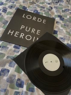 a black record sitting on top of a bed next to a sign that says lorde pure hero