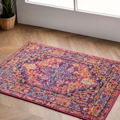 a colorful area rug on the floor in front of a window with potted plants