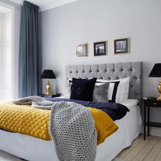 a bedroom with blue and yellow colors on the walls, white bedding, gray headboard