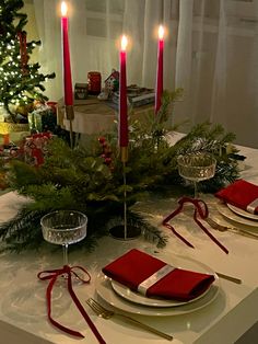 the table is set for christmas dinner with red napkins, silverware and candles