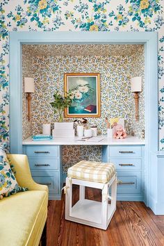 a room with blue and yellow flowers on the wall next to a vanity, stool and mirror