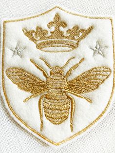 a white and gold bee with a crown on it's head in front of a white background