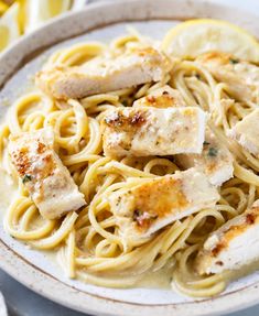 a plate of pasta with chicken and lemons on the side, ready to be eaten