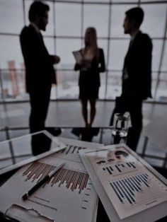 three business people standing in an office looking at papers on a table with pen and paper clippings