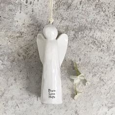 a ceramic angel ornament hanging from a hook on a concrete wall next to flowers