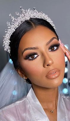 a woman in a bridal gown and tiara with her hands on her head