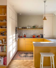 a kitchen with yellow cabinets and white counter tops, an island in the middle is surrounded by bookshelves