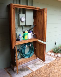 an open wooden box on the side of a house with hoses and other items in it