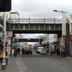 a busy city street with people walking on the sidewalk and cars driving under an overpass