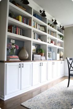 a room filled with lots of white bookshelves next to a dining room table