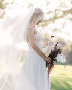 a woman in a white wedding dress holding a bridal bouquet and veil over her head