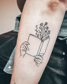 a person with a tattoo on their arm holding a book and flowers in its hand