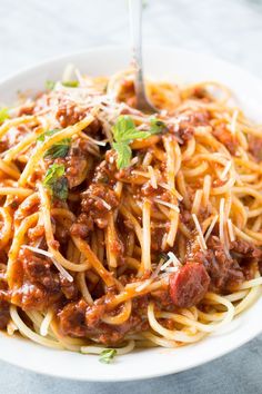 spaghetti with meat sauce and parmesan cheese in a white bowl on a table